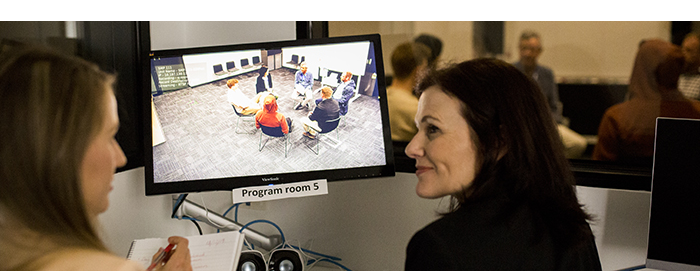 Two female clinicians watching a clinical session on a monitor.