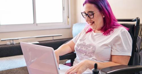 Woman with brightly coloured hair and glasses typing on a laptop